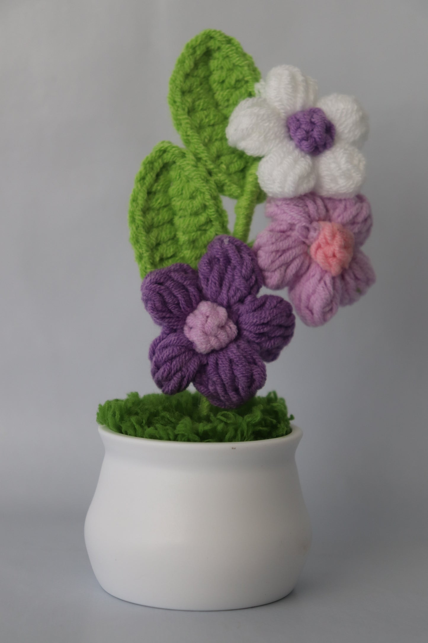 Crocheted flowers in white and purple, and with green leaves.