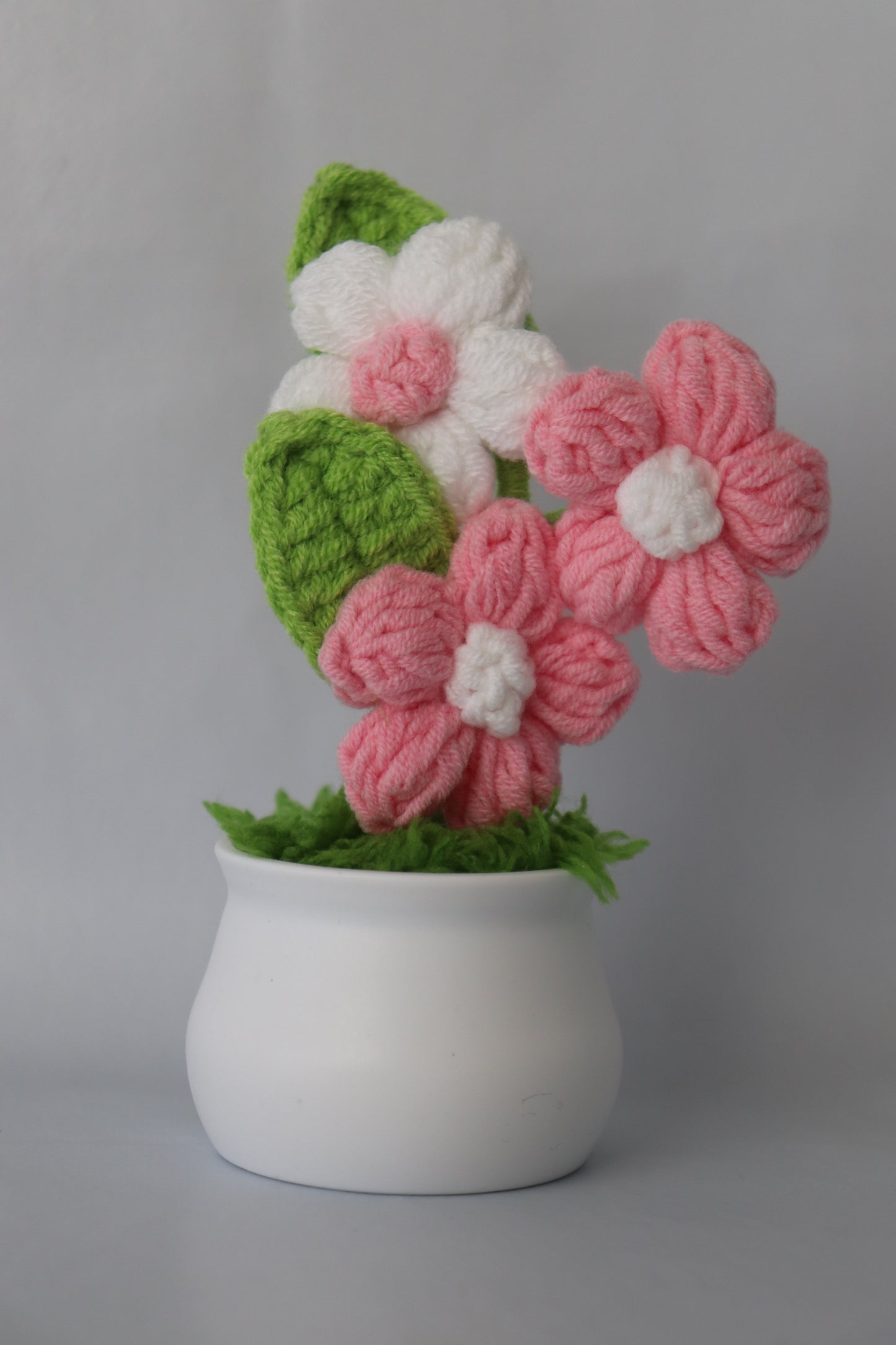 Knitted flowers in pink, white, and green on a gray background