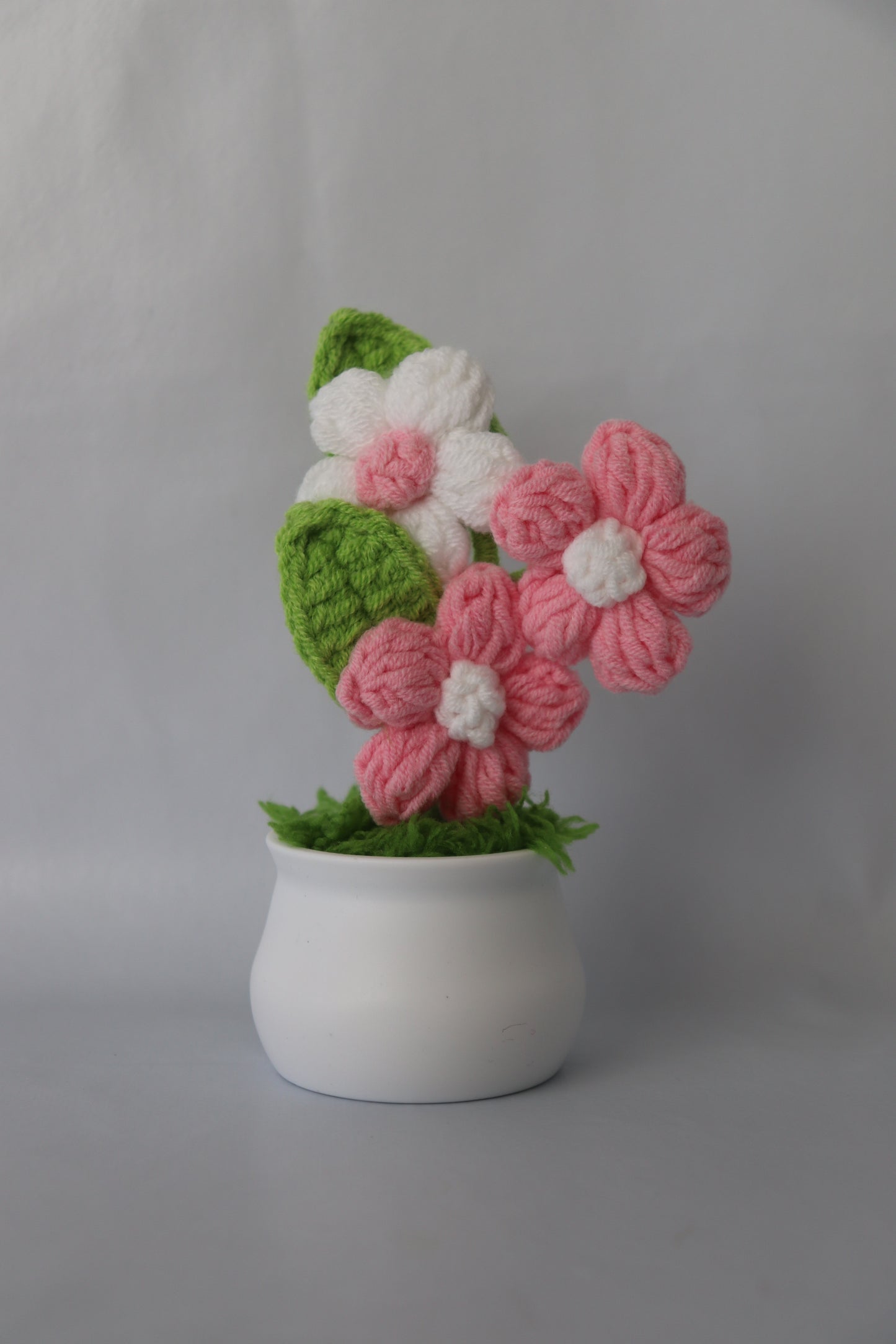Knitted flower arrangement in a white pot on a gray background